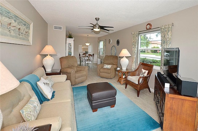 living room with ceiling fan, visible vents, and a textured ceiling