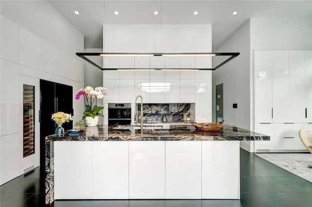 kitchen featuring oven, sink, dark stone countertops, and white cabinetry