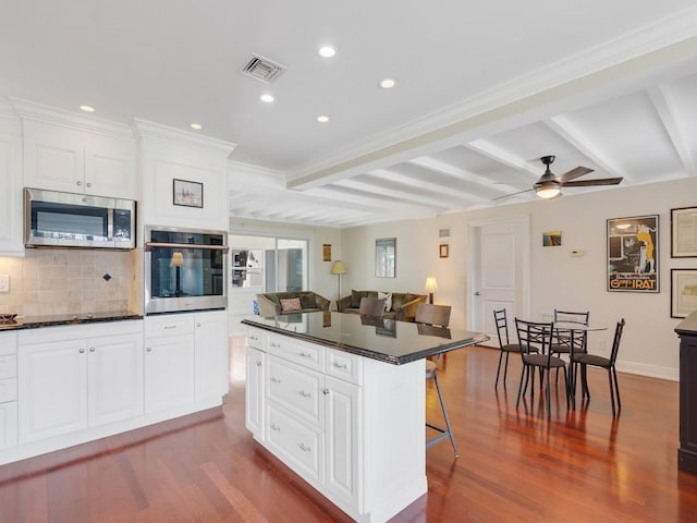 kitchen featuring a kitchen island, a breakfast bar, beamed ceiling, white cabinetry, and stainless steel appliances