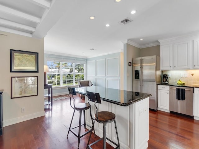 kitchen with a kitchen bar, a center island, dark stone counters, stainless steel appliances, and white cabinets