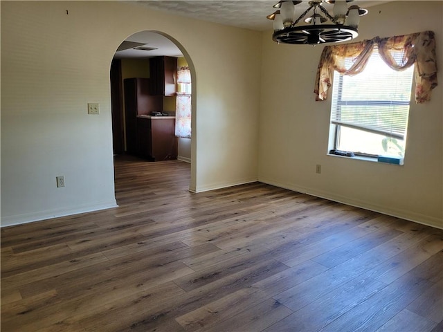 spare room with baseboards, an inviting chandelier, dark wood-type flooring, visible vents, and arched walkways