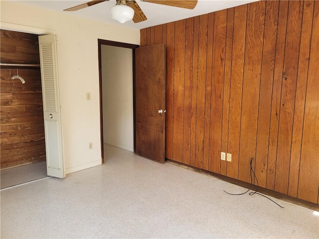 unfurnished bedroom featuring a closet, wooden walls, baseboards, and a ceiling fan