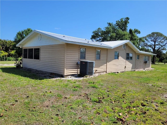 rear view of house featuring metal roof, central AC, and a lawn