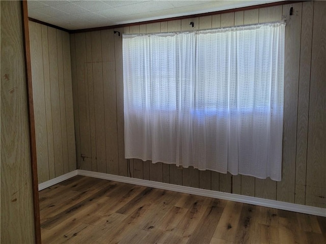 unfurnished room with wood walls, baseboards, and wood finished floors