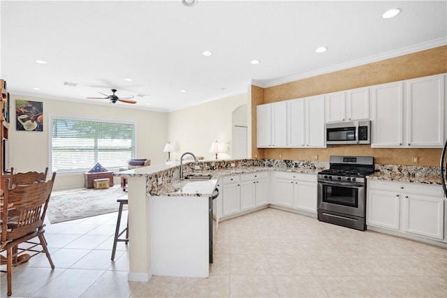 kitchen featuring kitchen peninsula, appliances with stainless steel finishes, light stone counters, white cabinets, and a breakfast bar area