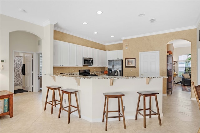 kitchen featuring white cabinets, stainless steel appliances, light stone counters, and a breakfast bar area