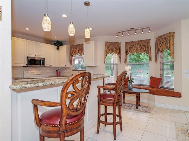 kitchen with light stone countertops, a kitchen breakfast bar, tasteful backsplash, electric stove, and hanging light fixtures