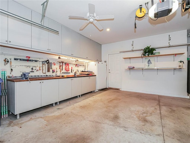 garage with a workshop area, ceiling fan, white fridge, and a garage door opener