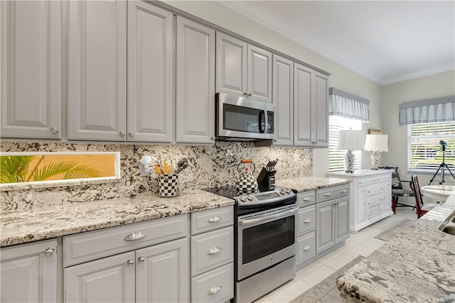 kitchen with light tile patterned flooring, gray cabinetry, decorative backsplash, stainless steel appliances, and crown molding