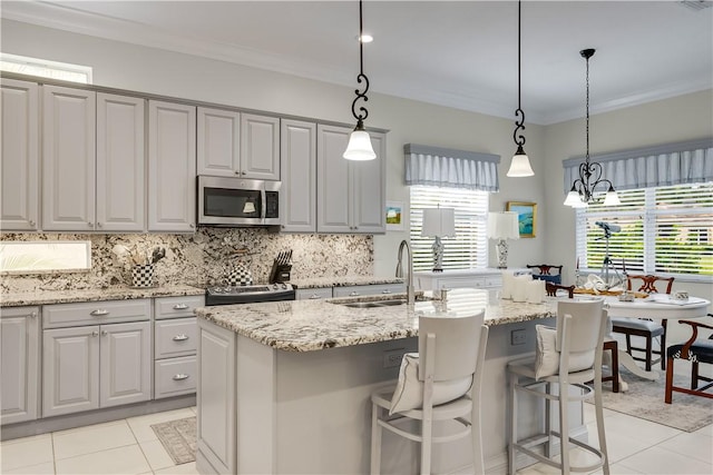 kitchen featuring sink, gray cabinetry, hanging light fixtures, a center island with sink, and appliances with stainless steel finishes