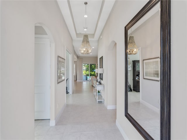 hall with a raised ceiling, light tile patterned flooring, and a notable chandelier