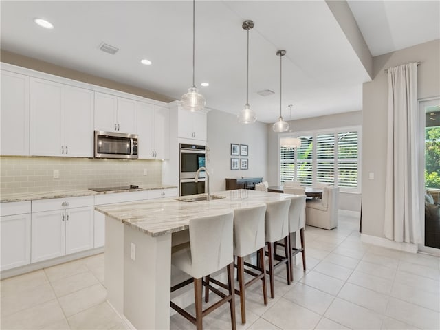 kitchen featuring an island with sink, stainless steel appliances, decorative backsplash, decorative light fixtures, and white cabinets