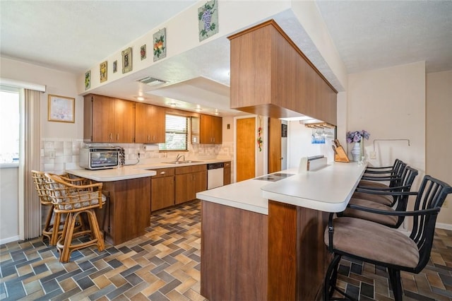 6001 Palm Dr, Fort Pierce, FL 34982 - kitchen featuring a peninsula, decorative backsplash, brown cabinetry, and dishwashing machine