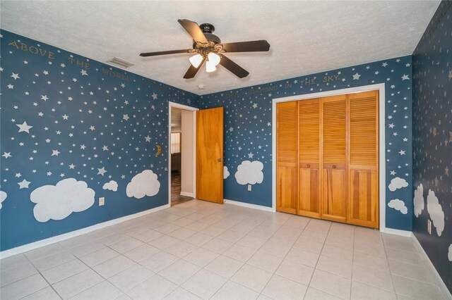 6001 Palm Dr, Fort Pierce, FL 34982 - unfurnished bedroom featuring a textured ceiling, a ceiling fan, tile patterned flooring, a closet, and wallpapered walls