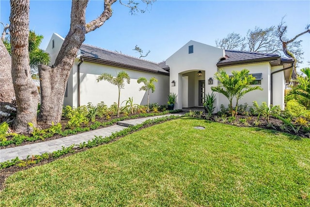 view of front of home with a tile roof, a front yard, and stucco siding