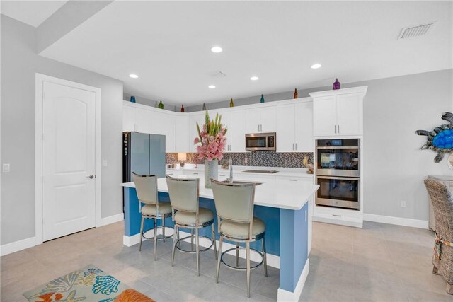 kitchen featuring appliances with stainless steel finishes, tasteful backsplash, a breakfast bar, a center island with sink, and white cabinetry