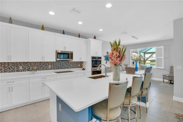 kitchen with white cabinets, sink, stainless steel appliances, and an island with sink