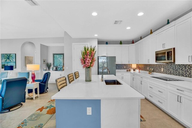 kitchen with backsplash, stainless steel appliances, sink, a center island with sink, and white cabinetry