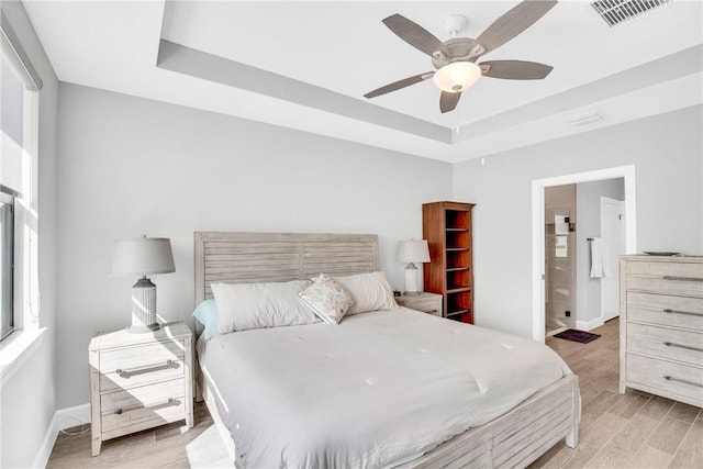 bedroom with visible vents, ceiling fan, a raised ceiling, baseboards, and light wood-style floors