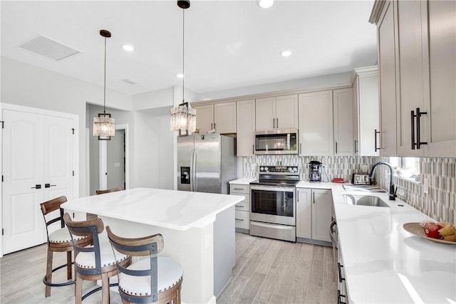 kitchen featuring light wood-style flooring, a sink, stainless steel appliances, tasteful backsplash, and gray cabinets