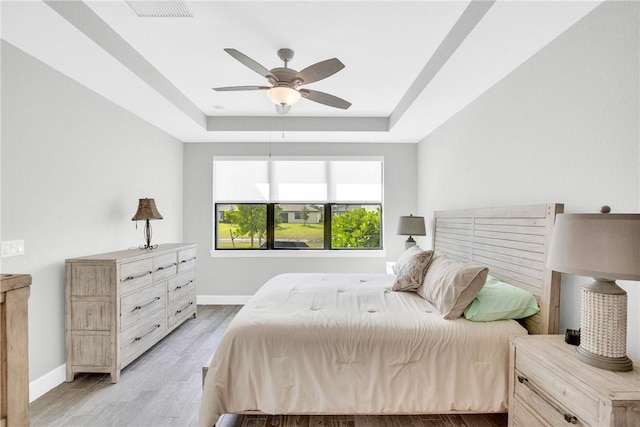 bedroom featuring light wood-style flooring, baseboards, ceiling fan, visible vents, and a raised ceiling
