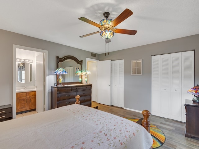 bedroom with connected bathroom, two closets, ceiling fan, and light wood-type flooring