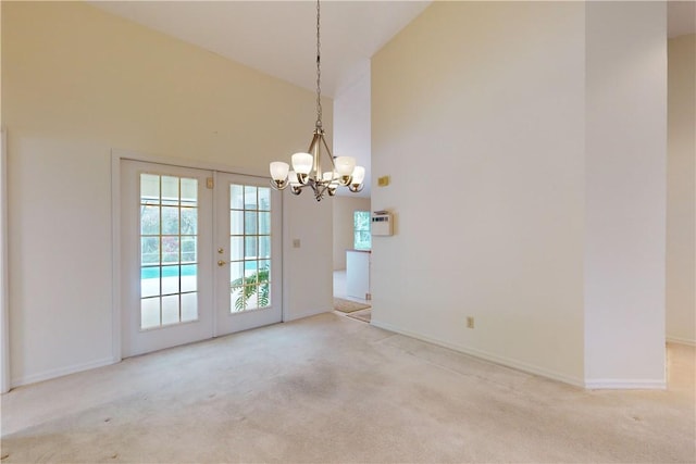 unfurnished room with french doors, light colored carpet, an inviting chandelier, and high vaulted ceiling