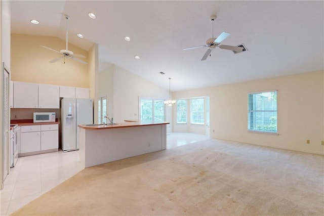 unfurnished living room featuring ceiling fan with notable chandelier, light colored carpet, and high vaulted ceiling