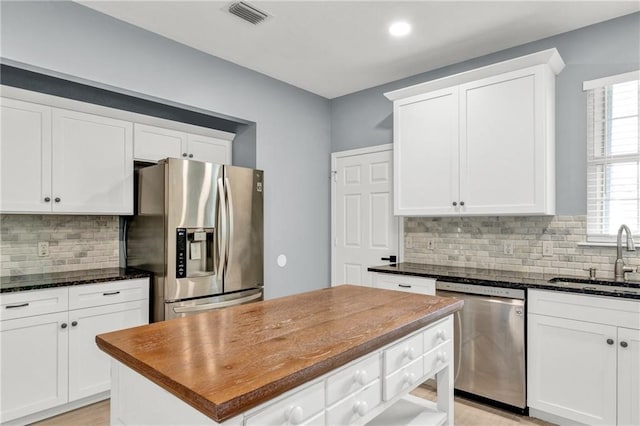 kitchen with white cabinets, appliances with stainless steel finishes, dark stone countertops, and sink