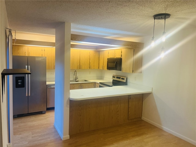 kitchen with kitchen peninsula, appliances with stainless steel finishes, a textured ceiling, sink, and light hardwood / wood-style flooring