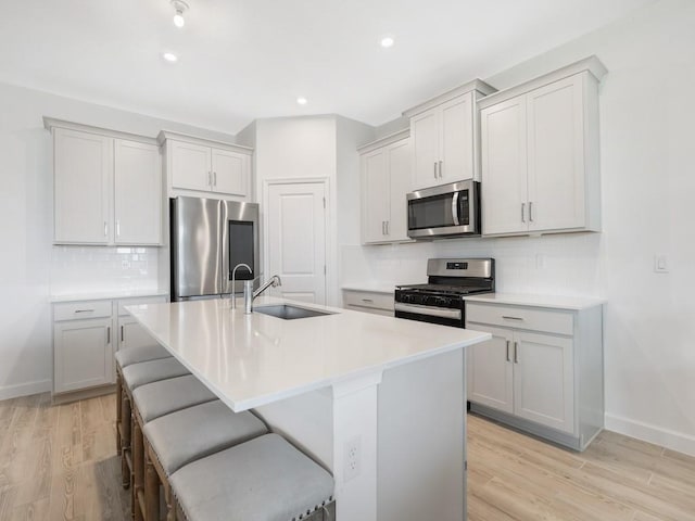 kitchen with stainless steel appliances, a sink, a kitchen breakfast bar, light wood-type flooring, and a center island with sink