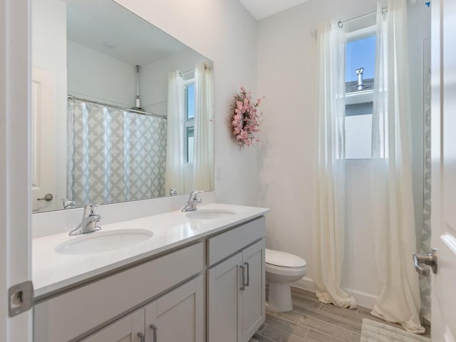 full bathroom with toilet, double vanity, a sink, and wood finished floors