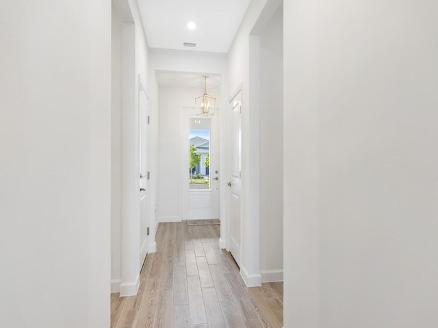 hallway featuring light wood-style floors, visible vents, a notable chandelier, and baseboards