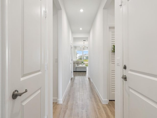 hall with recessed lighting, baseboards, light wood finished floors, and an inviting chandelier