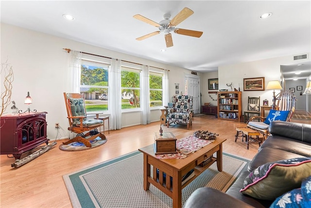 living room featuring ceiling fan, light hardwood / wood-style floors, and a wood stove