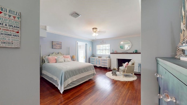 bedroom with a stone fireplace, ornamental molding, and dark hardwood / wood-style floors