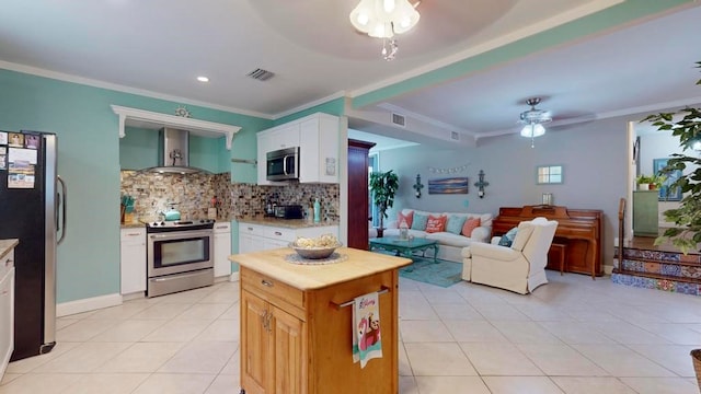 kitchen with wall chimney range hood, appliances with stainless steel finishes, ceiling fan, and white cabinets