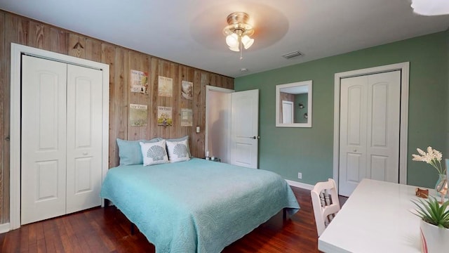 bedroom with multiple closets, wooden walls, ceiling fan, and dark hardwood / wood-style floors