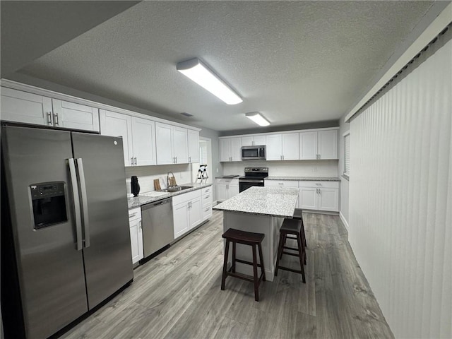 kitchen featuring a breakfast bar, a sink, stainless steel appliances, white cabinets, and light wood finished floors