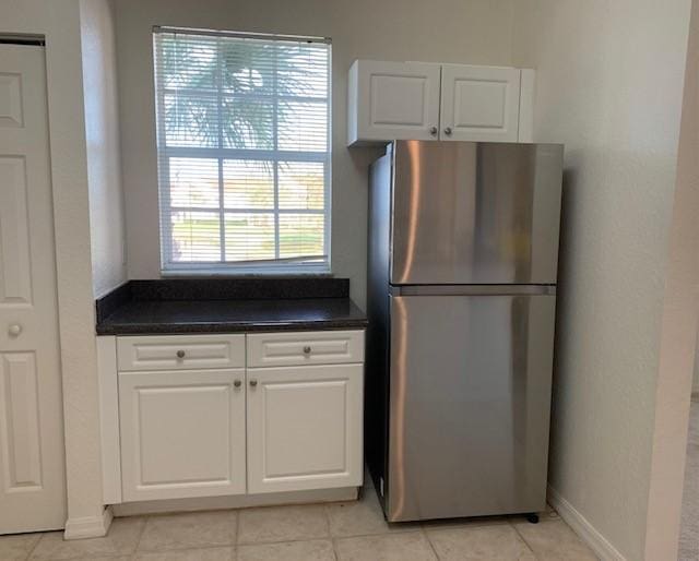 kitchen with plenty of natural light, stainless steel fridge, light tile patterned floors, and white cabinets