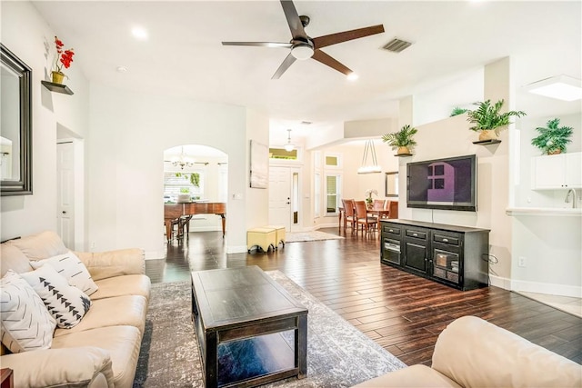 living area featuring arched walkways, ceiling fan with notable chandelier, dark wood-type flooring, visible vents, and baseboards