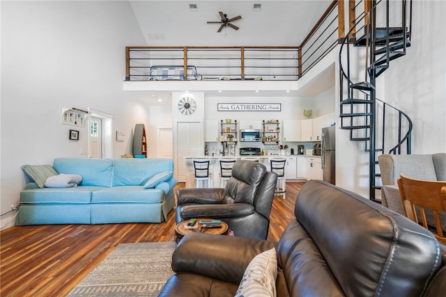 living room featuring ceiling fan, a towering ceiling, and wood-type flooring