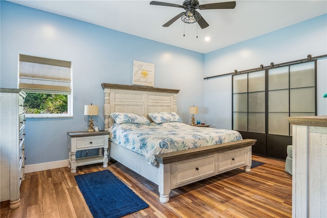 bedroom featuring dark wood-type flooring, a barn door, and ceiling fan