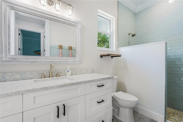 bathroom with vanity, toilet, a tile shower, and ornamental molding