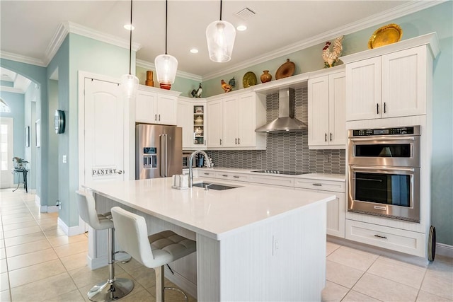 kitchen with sink, a center island with sink, pendant lighting, stainless steel appliances, and wall chimney range hood