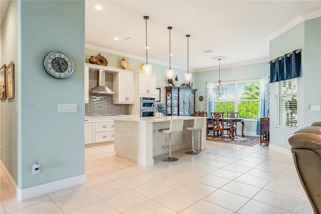 kitchen featuring a kitchen breakfast bar, wall chimney range hood, pendant lighting, white cabinetry, and an island with sink