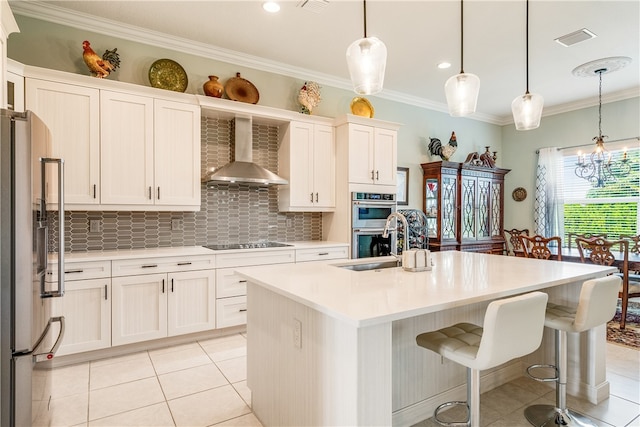 kitchen featuring decorative light fixtures, stainless steel appliances, a kitchen island with sink, and wall chimney exhaust hood