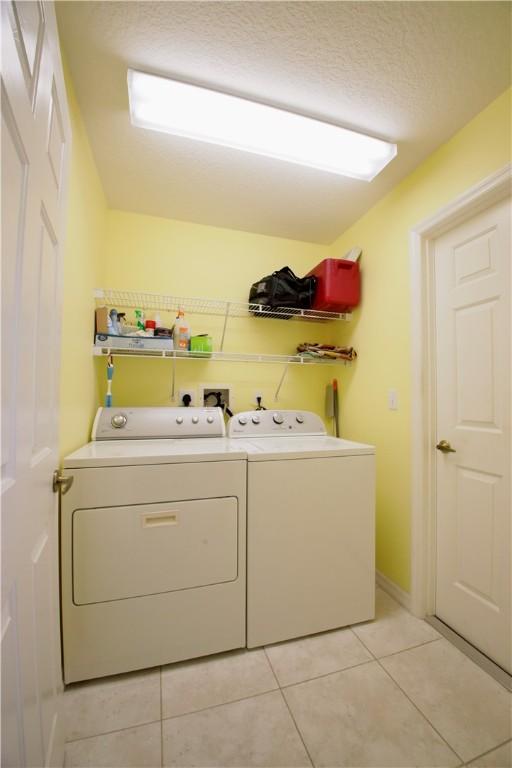 clothes washing area with washing machine and dryer, light tile patterned flooring, and a textured ceiling