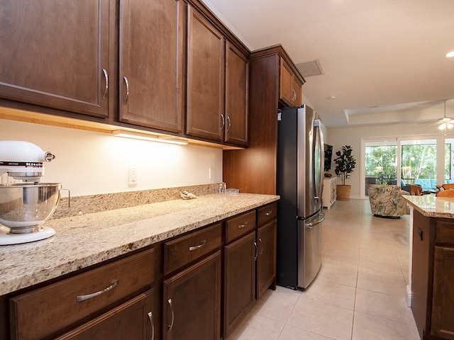 kitchen featuring ceiling fan, light stone countertops, stainless steel refrigerator, and dark brown cabinets