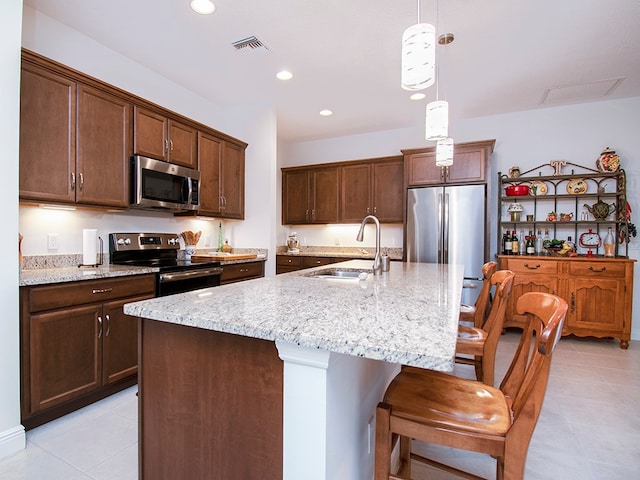 kitchen with stainless steel appliances, a center island with sink, sink, light stone counters, and hanging light fixtures